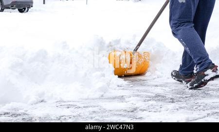 Mann schaufelt Schnee von seiner Auffahrt nach einem Wintersturm in Kanada. Mann mit Schneeschaufel reinigt im Winter Gehsteige. Winterzeit. Stockfoto