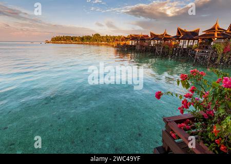 Hütten auf Stelzen sitzen über klarem tropischem Wasser in einem luxuriösen Resort-Hotel, während die Sonne untergeht Stockfoto