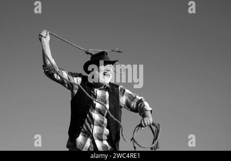 Älterer westlicher Cowboy, der Lassosseil wirft. Bärtiger Wilder Westmann mit brauner Jacke und Hut, der Pferd oder Kuh fängt. Rodeo oder Ranch. Stockfoto