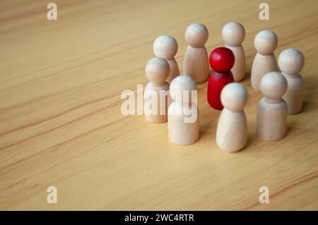 Rote Holzpuppe umgeben von anderen Puppen. Repräsentiert entweder Diskussionen, Führungsqualitäten oder Belästigungen. Stockfoto