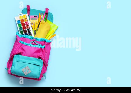 Stylischer Schulrucksack mit verschiedenen Schreibwaren auf blauem Hintergrund Stockfoto