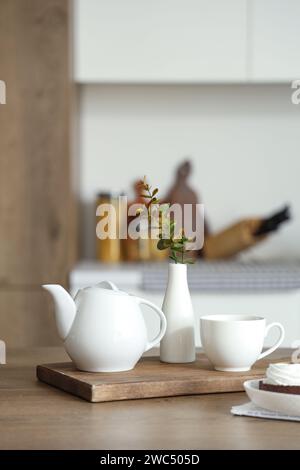 Moderne Frühstückseinrichtung mit Teekanne, Tasse und Eukalyptuszweigen in Vase auf Holztisch Stockfoto