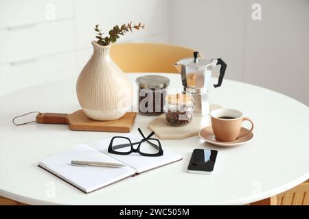 Frühstückseinrichtung mit Geysir-Kaffeemaschine, Tasse Espresso, Notebook und Mobiltelefon in der Küche Stockfoto