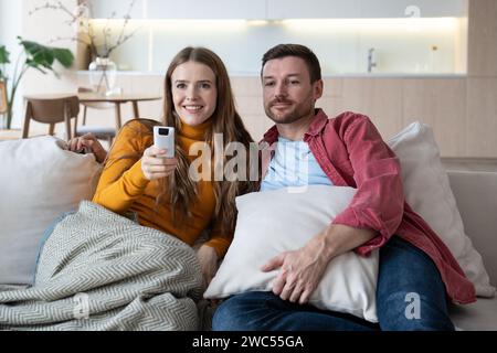 Ein Mann und eine Frau, die sich die TV-Show anschauen, sitzen auf der Couch zu Hause und wechselten am Wochenende den Sender Stockfoto