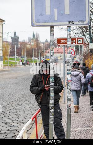 Ein Obdachloser mit Telefon auf der Straße der alten mittelalterlichen Stadt Prag im Winter. Er war konzentriert und schaute ins Telefon Stockfoto