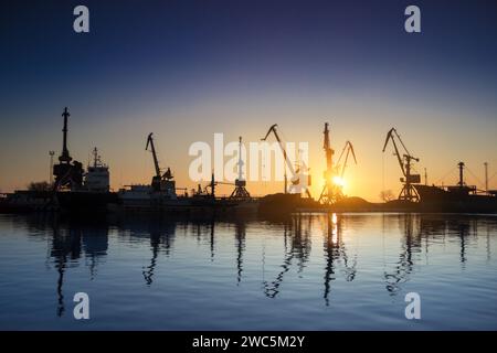 Sonnenuntergang Silhouetten Frachtschiffe, Kräne am Seehafen. Industrie lädt Fracht am Dock. Handel, Verkehrsinfrastruktur. Maritime Logistik, global Stockfoto