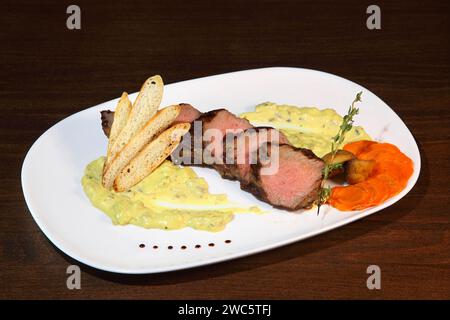 Mittelgroßer Braten, in Stücke geschnitten in cremiger Pilzsauce. Steak wird auf einem weißen Teller und Holztisch serviert. Stockfoto