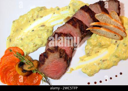 Mittelgroßer Braten, in Stücke geschnitten in cremiger Pilzsauce. Steak wird auf einem weißen Teller und Holztisch serviert. Stockfoto