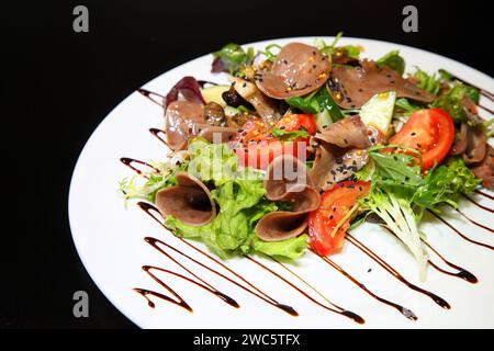 Salat mit Rindfleisch, Zunge mit Gemüse und Kräutern, gekleidet mit Soße auf einer weißen Platte. Stockfoto