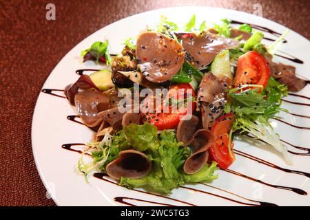 Salat mit Rindfleisch, Zunge mit Gemüse und Kräutern, gekleidet mit Soße auf einer weißen Platte. Stockfoto