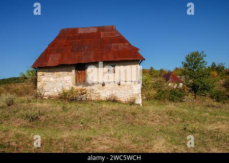 Alte Steinhäuser in den Bergen. Traditionelles Steinhaus in Bosnien und Herzegowina. Rostiges Blechdach auf verlassenem Haus. Stockfoto