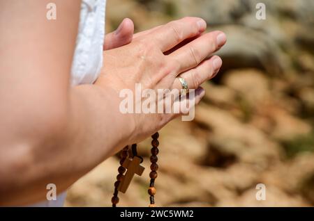 Christliche Frau betet vor der Kathedrale. Hände des Pilgers, der den Rosenkranz hält. Frau mit gekreuzten Händen. Stockfoto