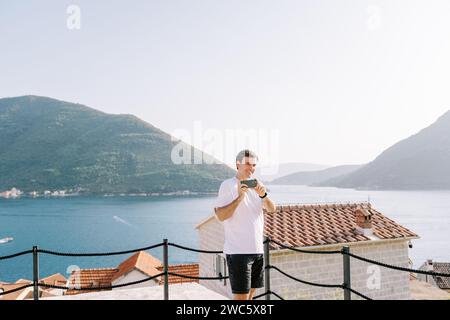 Der Mann schießt mit einem Smartphone, während er auf einer Plattform über dem Meer steht Stockfoto
