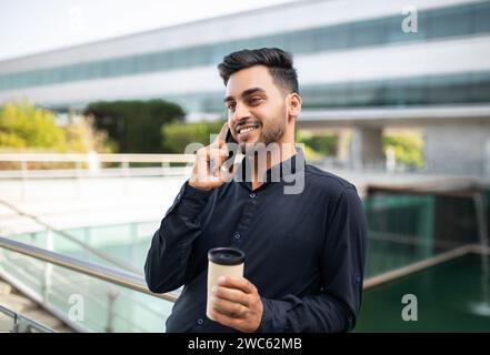 Glücklicher junger Angestellter, der draußen auf dem Smartphone einen Kaffee hält Stockfoto