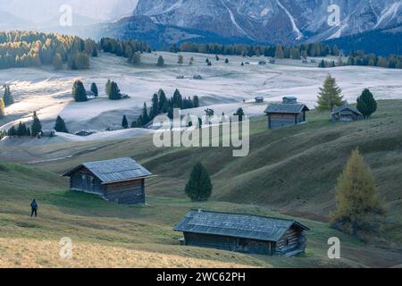 Wanderer auf wunderschöner herbstlicher Hochalpenweide mit Hütten während Sonnenaufgang, Dolomiten, Italien Stockfoto