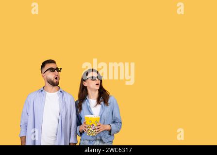 Überraschendes Paar in 3D-Brille mit Popcorn, das begeistert aufblickt Stockfoto