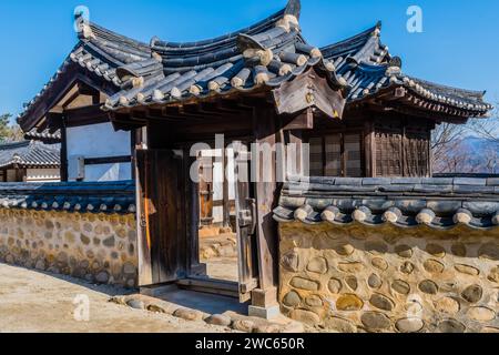 Traditionelles Tor mit Keramikfliesendach in einer Schlammsteinwand mit koreanischer Architektur im öffentlichen Park Stockfoto