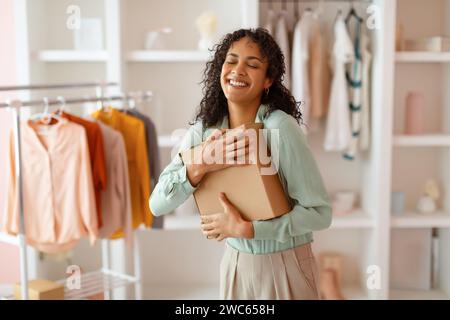 Glückliche Geschäftsfrau, die ein Paket in ihrem Büro umarmt Stockfoto