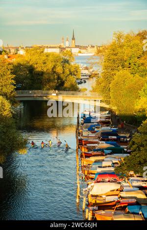 Leute auf dem Kajak. Klassische Holzboote legen in Stockholm an, mit Blick auf die Altstadt und die Riddarholmen im Hintergrund. Warmes, farbenfrohes Sommerlicht. Stockfoto