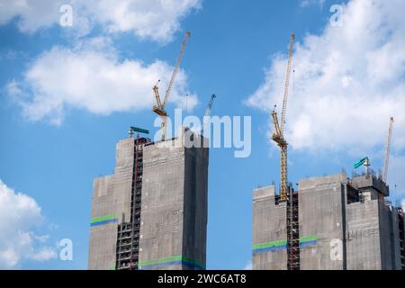 Zwei stehende Hochhäuser im Gerüst sind mit technischem Gewebe bedeckt, mit einer Schutzplane mit Kränen auf der Oberseite, gegen den Rücken Stockfoto