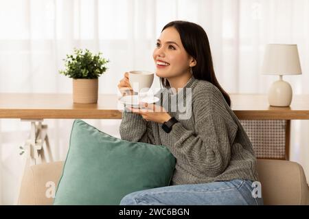 Lächelnde brünette Dame, die ein heißes Getränk trinkt und sich während ihrer Pause entspannt Stockfoto