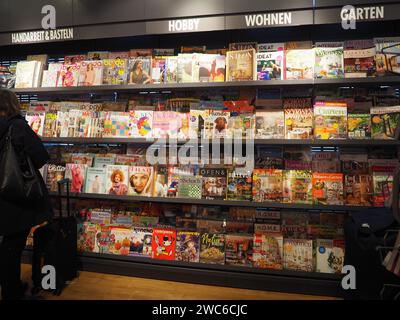 Schräge Ansicht des Zeitschriftenregals im Bahnhofsbuchladen mit Frau, Koffer, Sektion Kunsthandwerk, Hobbys, Leben, Garten, Deutsch, Reisezeitschriften Stockfoto