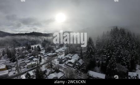 Eine erhöhte Perspektive fängt die malerische Schönheit einer charmanten kleinen Stadt ein, eingebettet in majestätische schneebedeckte Berge und üppige Bäume Stockfoto