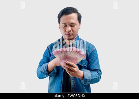 Junger asiatischer Mann mit besorgtem Gesichtsausdruck, während er Papiergeld hält Stockfoto