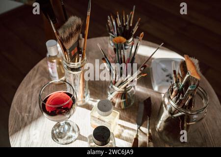 Draufsicht auf einen Tisch mit Malwerkzeugen, Pinseln, Öl, Farben und Rotweinglas Stockfoto