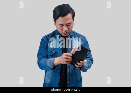 Junger asiatischer Mann mit schockiertem Gesichtsausdruck, während er seine Brieftasche hält und das Geld zählt Stockfoto
