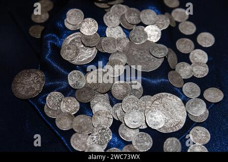 Alte Silbermünzen liegen auf tiefblauer Seide, Nahaufnahme mit selektivem Weichfokus Stockfoto
