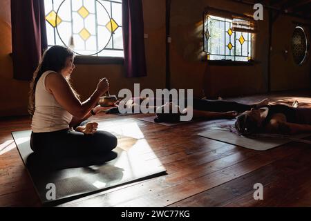 Frau in Lotusposition, die eine Meditationssitzung führt. Entspannender Moment nach dem Gruppen-Yoga-Kurs. Leuchtender Kontrast. Stockfoto