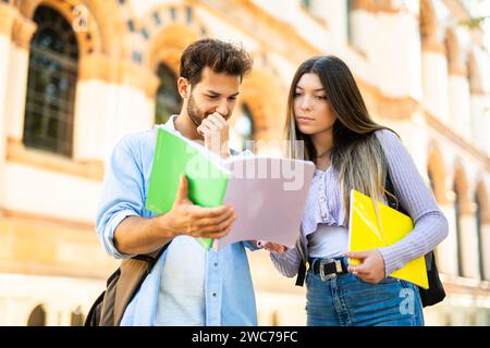 Zwei junge Studenten, die zusammen Notizen lesen, vor einem Campus-Gebäude Stockfoto