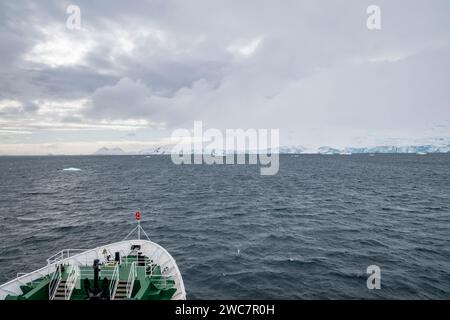 Das Schiff fährt an einem bewölkten Tag im Frühling in die Bucht von Brialmont in der antarktis und an der schneebedeckten Küste mit Eisbögen und Höhlen Stockfoto