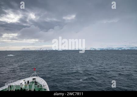 Das Schiff fährt an einem bewölkten Tag im Frühling in die Bucht von Brialmont in der antarktis und an der schneebedeckten Küste mit Eisbögen und Höhlen Stockfoto