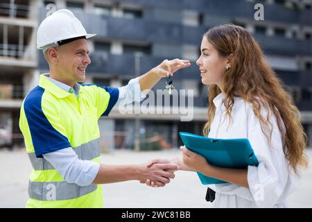 Baumeister gibt der Frau auf der Baustelle Schlüssel Stockfoto