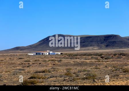 Kleines Haus, das allein in einer Wüstenlandschaft mit Bergen im Hintergrund steht, El Cotillo, Fuerteventura, November 2023 Stockfoto