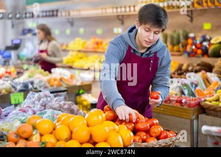 Junger männlicher Verkäufer, der Tomaten hält, die auf dem Lebensmittelmarkt stehen Stockfoto