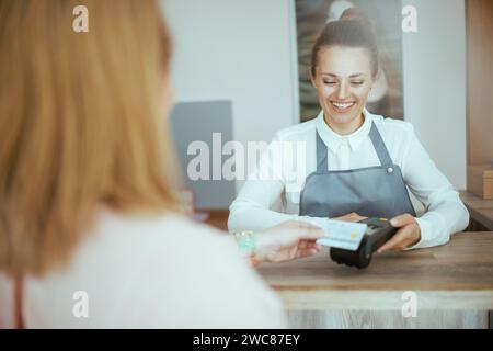 40 Jahre alter Friseurangestellter in einem modernen Schönheitssalon, der Kunde akzeptiert Kreditkartenzahlungen über das Terminal an der Rezeption. Stockfoto