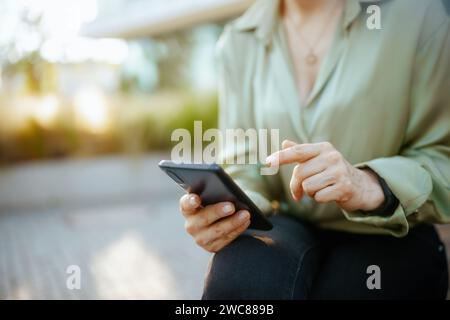 Nahaufnahme einer Geschäftsfrau im Geschäftsviertel in grüner Bluse und Brille mit Smartphone. Stockfoto