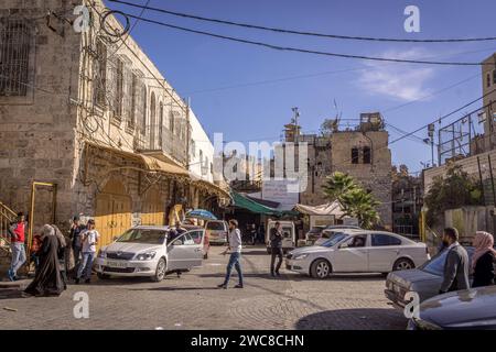 Die Palästinenser laufen in der Stadt Hebron, Westufer (Palästina) mit den alten Steinhäusern und Schild „Willkommen in der Altstadt Hebrons“ (in Stockfoto