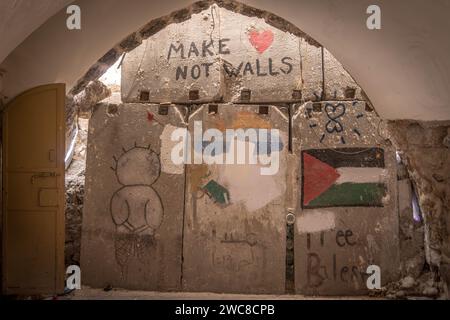 Die Betonbarrikaden in der Altstadt von Hebron mit palästinensischer Flagge, Worten „Make love not war“ und Wandgemälden auf dem bo Stockfoto