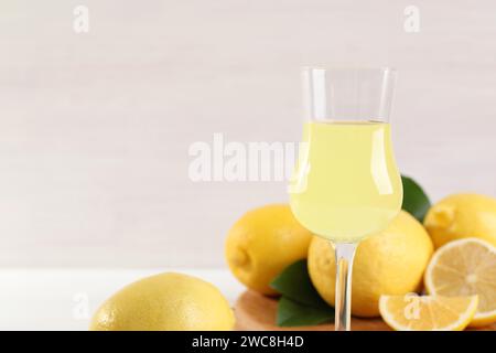 Likörglas mit leckerem Limoncello, Zitronen und grünen Blättern auf dem Tisch, Nahaufnahme. Leerzeichen für Text Stockfoto