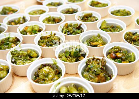 Zahlreiche weiße Keramikramekins gefüllt mit Meeresfrüchten, in pulsierender Pesto-Sauce geworfen, auf einer Holzoberfläche ausgestellt. Stockfoto