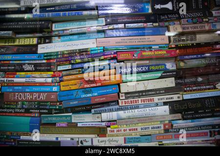 Ein Stapel gebrauchter, gebundener und gebundener Bücher stapelt sich vor einem transparenten Fenster in einem Second-Hand-Buchladen. Stockfoto