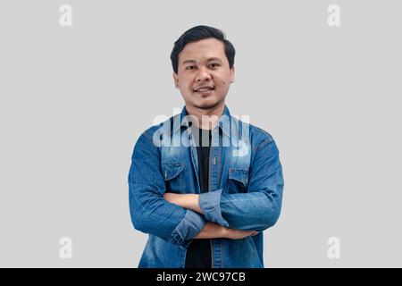 Junger asiatischer Mann faltete Arme und blickte in die Kamera mit glücklichem Gesichtsausdruck auf isoliertem Hintergrund Stockfoto