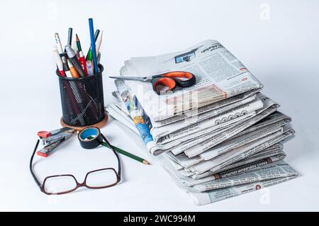 Stapel von Zeitungen, die gelesen werden müssen, um Informationen über Geschäfts- und Finanznachrichten zu erhalten, sowie Schreibwaren und Brillen auf dem Tisch Stockfoto