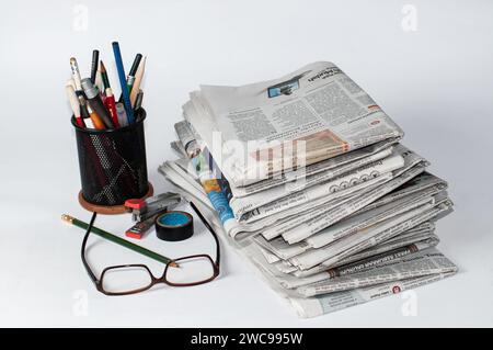 Stapel von Zeitungen, die gelesen werden müssen, um Informationen über Geschäfts- und Finanznachrichten zu erhalten, sowie Schreibwaren und Brillen auf dem Tisch Stockfoto