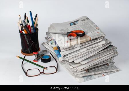 Stapel von Zeitungen, die gelesen werden müssen, um Informationen über Geschäfts- und Finanznachrichten zu erhalten, sowie Schreibwaren und Brillen auf dem Tisch Stockfoto