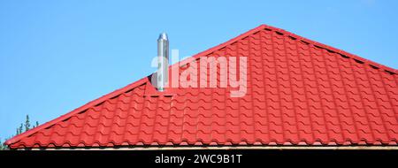 Eine Nahaufnahme eines roten Metalldachs mit koaxialem Kamin, Edelstahl-Metallschornstein, Rauchrohr gegen den blauen Himmel. Stockfoto